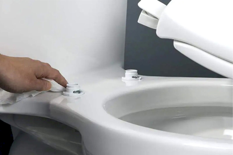 ay người dùng khăn giấy lau sạch vị trí lắp bản lề nắp bồn cầu Kohler trắng.