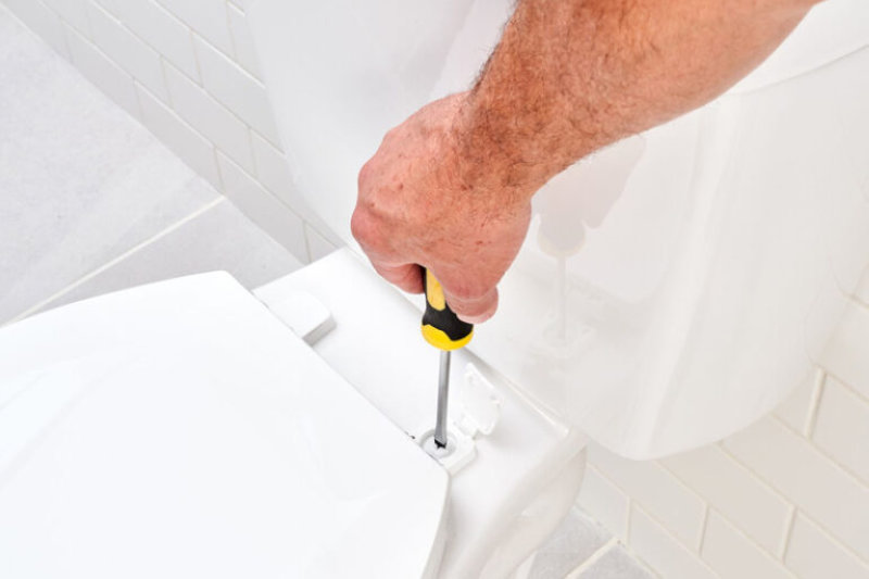 Sửa bồn cầu với thao tác cẩn thận bằng tua vít để cố định lại nắp ngồi trong phòng vệ sinh gia đình.