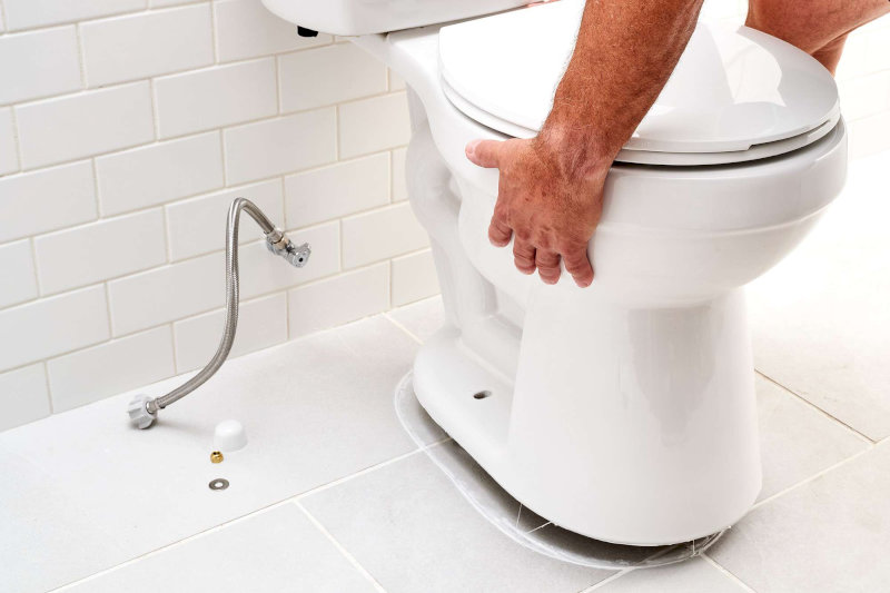 Người dùng đang căn chỉnh bồn cầu vào vị trí gắn sáp trước khi bắt vít cố định trên sàn nhà vệ sinh