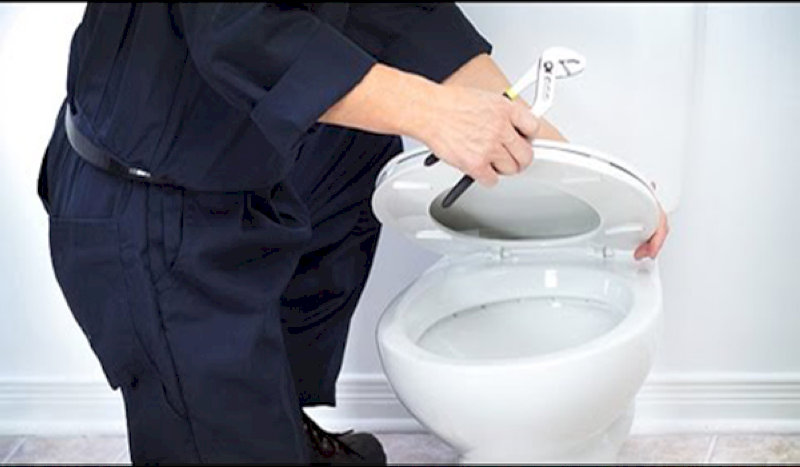  Người thợ dùng cờ lê siết chặt nắp bồn cầu trong quá trình lắp đặt thiết bị vệ sinh