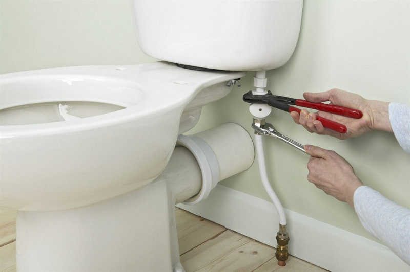Kỹ thuật viên đang dùng mỏ lết để siết chặt ống cấp nước dưới két bồn cầu
