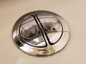Nút nhấn xả bồn cầu màu bạc, thiết kế hai chế độ xả tiết kiệm nước.
