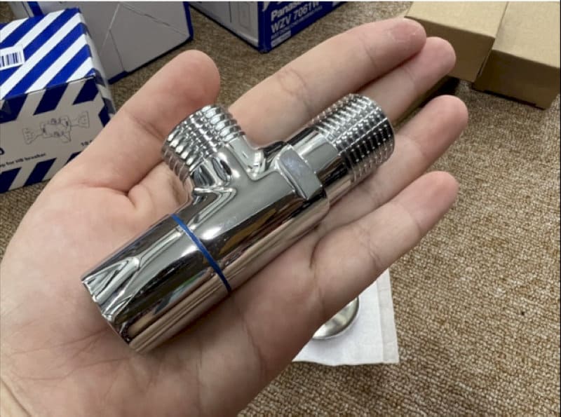 Van chia chữ T inox sáng bóng, nhỏ gọn, được cầm trên bàn tay người dùng.