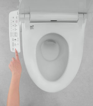 Tay người dùng nhấn nút trên bảng điều khiển nắp bồn cầu màu trắng.